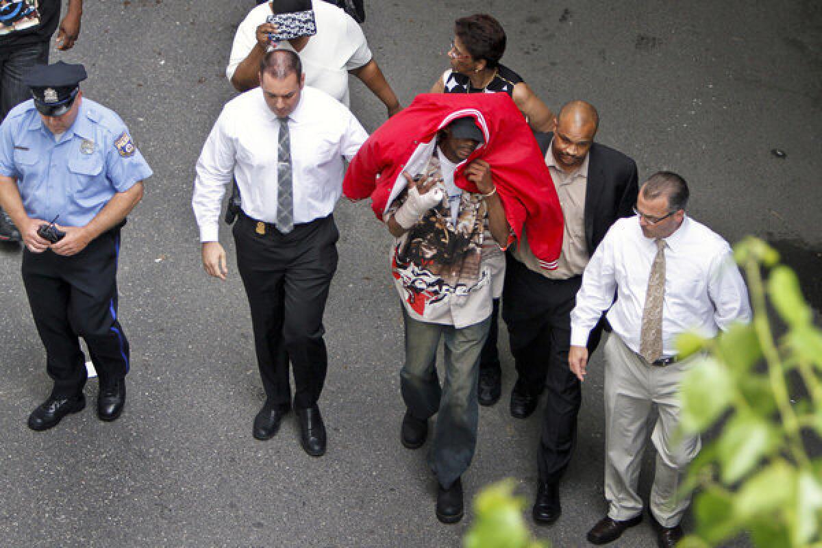 Sean Benschop, center, with a red jacket over his head, walks with investigators toward the Philadelphia Police Department's Central Detectives Division. He turned himself in to face charges, police said.