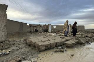 Personas permanecen de pie sobre un muro caído de su vivienda, que sufrió daños debido a las fuertes lluvias en un área cerca de Chaman, Pakistán, el jueves 18 de abril de 2024. (AP Foto/Habib Ullah)