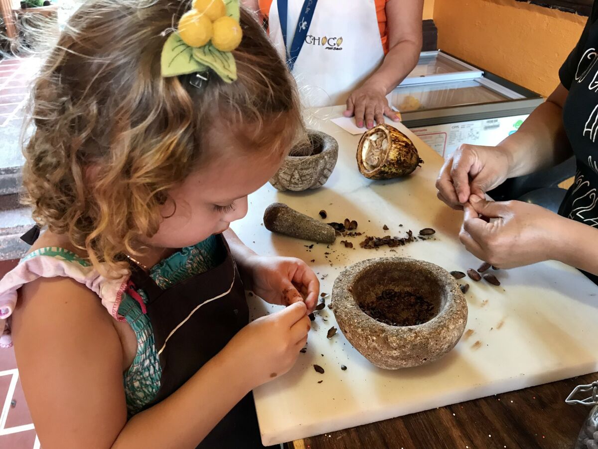 The reporter's daughter, Cora, separates the hulls from the interior nibs of roasted cocoa beans, before grinding them with a pestle into a smooth paste at the Choco Museo in Antigua, Guatemala