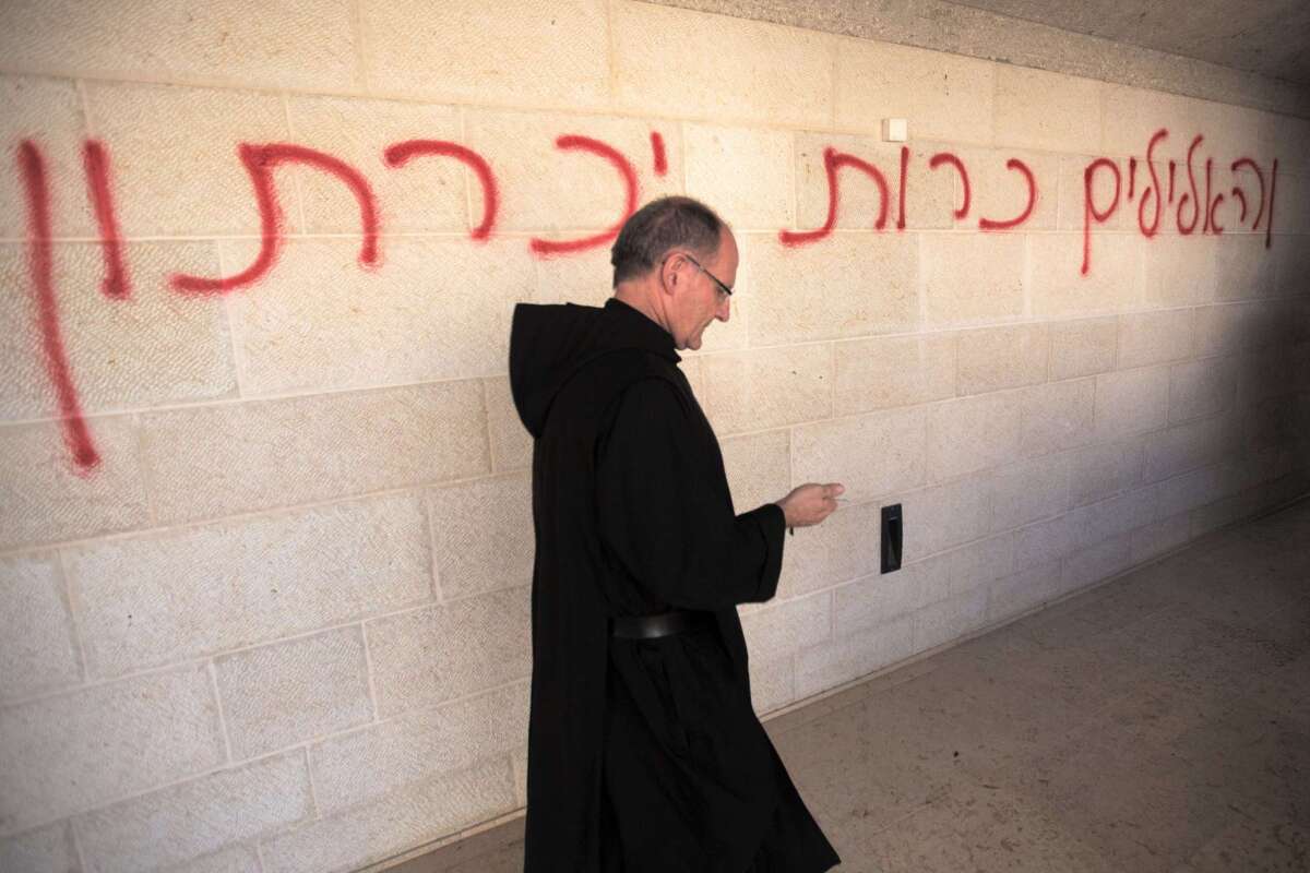 A priest walks past graffiti reading in Hebrew "idols will be cast out" at the Church of the Multiplication of Loaves and Fishes on Thursday.