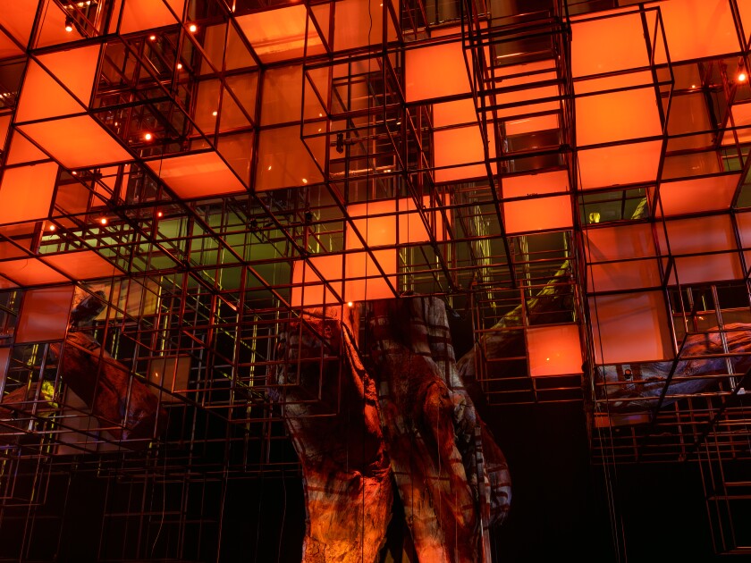 A sculpture composed of a trunk-like structure bearing branches of red, geometric lights, is seen in a darkened space.