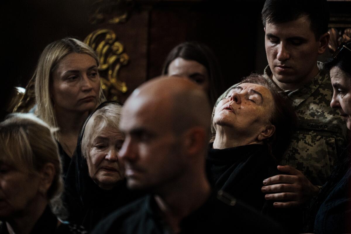 A woman leans her head against a man in uniform amid a funeral gathering