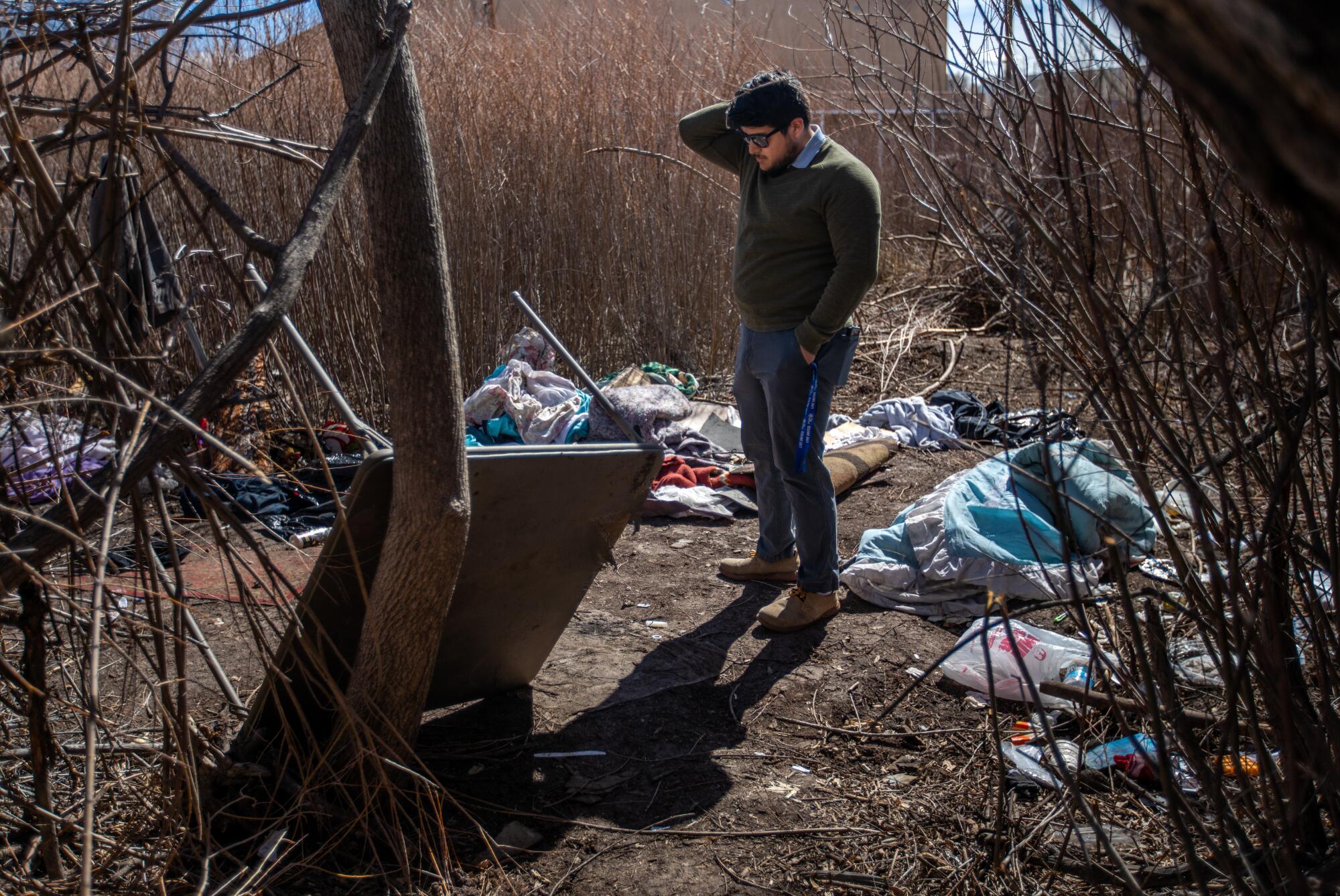 A man stands amid debris at a homeless camp 