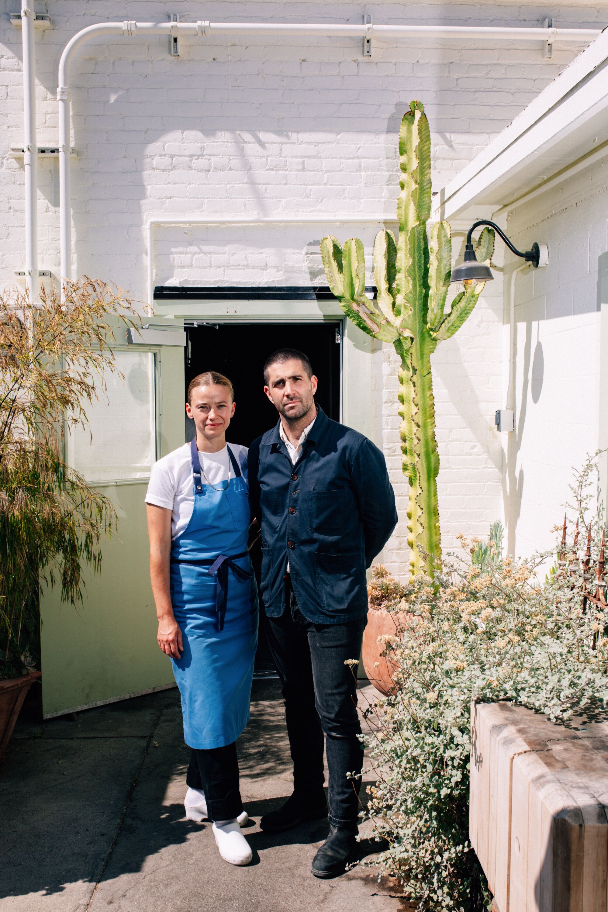 A man and a woman standing outside a white building and some cacti.