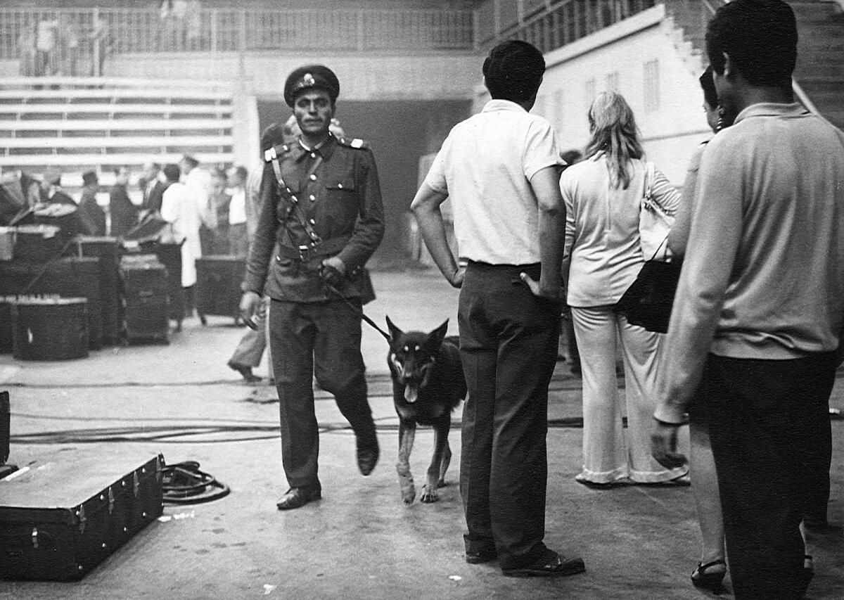 A man in uniform with a guard dog on a leash passes through an auditorium.