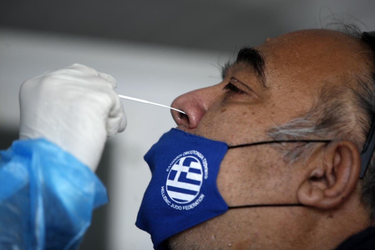 A medical staff member from the National Health Organization (EODY) conducts a rapid COVID test on a man, wearing a face mask with the Greek flag, in Athens, Thursday, Nov. 5, 2020. Greek Prime Minister Kyriakos Mitsotakis has announced a nationwide three-week lockdown starting Saturday morning, saying that the increase in the coronavirus infections must be stopped before Greece's health care system comes under "unbearable" pressure. (AP Photo/Thanassis Stavrakis)