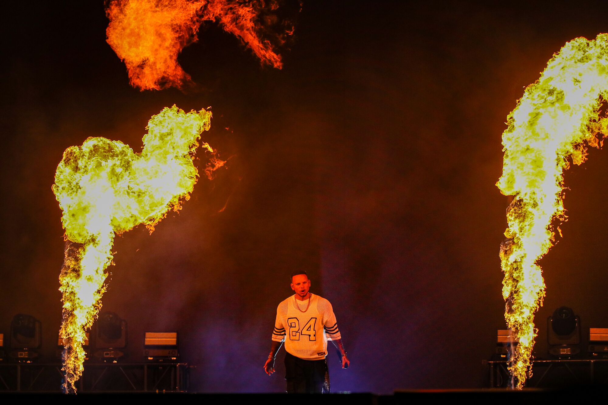 A man in a sports jersey stands on stage while flanked by tall vertical jets of fire.