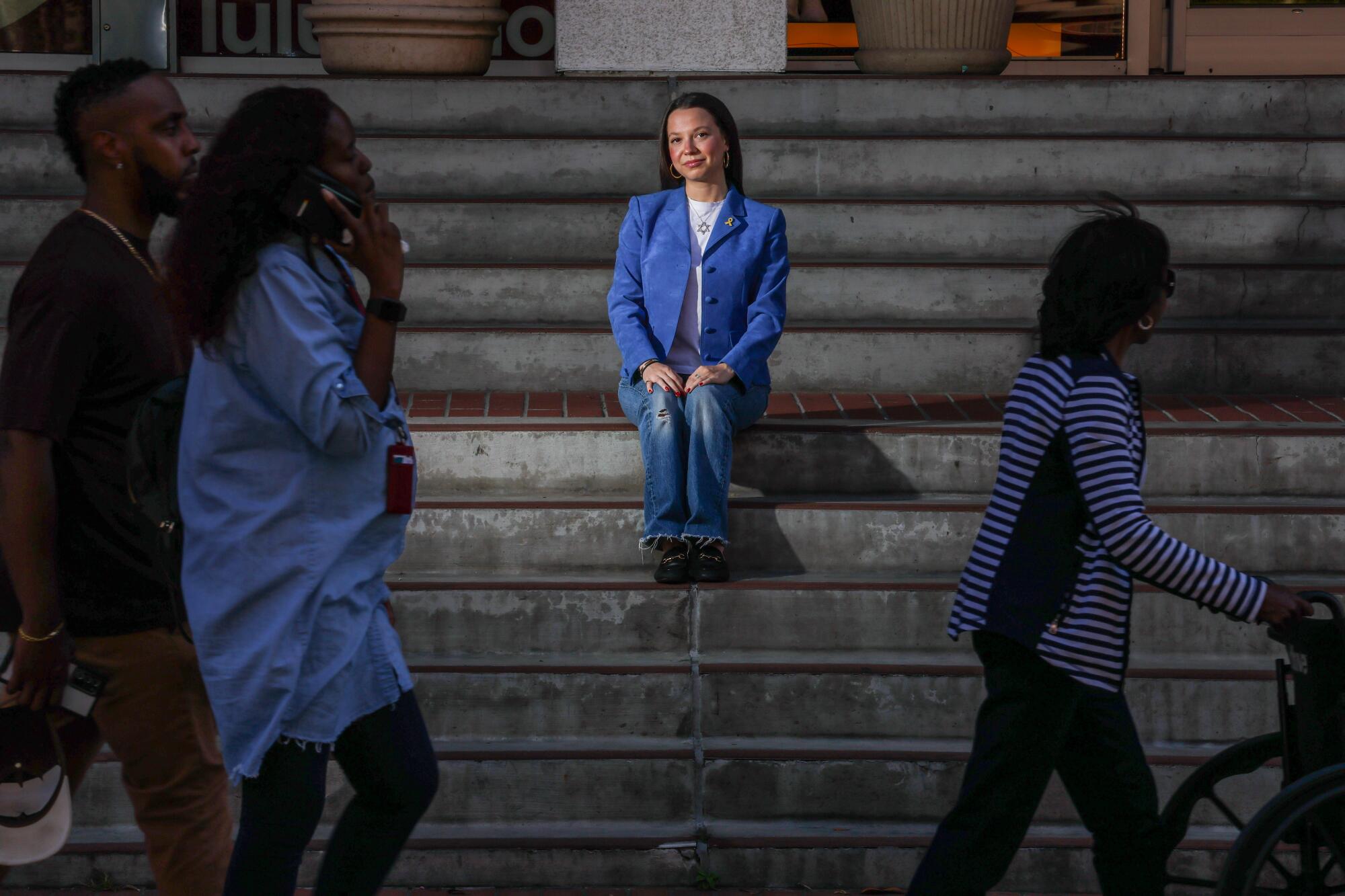 USC alumna Alyssa Wallack sits for a portrait on steps as people walk by