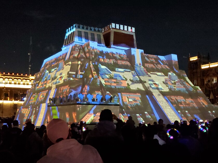 Ein hell erleuchtetes Kunstwerk, das nachts gezeigt wird, ist von einer Menschenmenge umgeben.