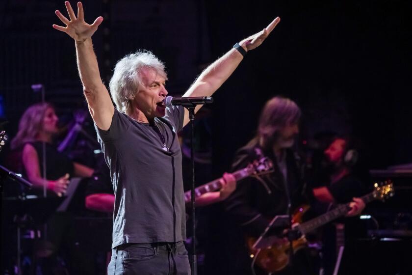 A man with white hair raising his arms into the air and singing into a microphone