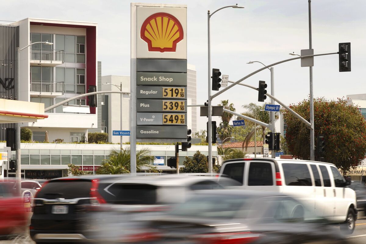 Cars drive past a gas station sign with prices from $5.19 a gallon to $5.49 a gallon