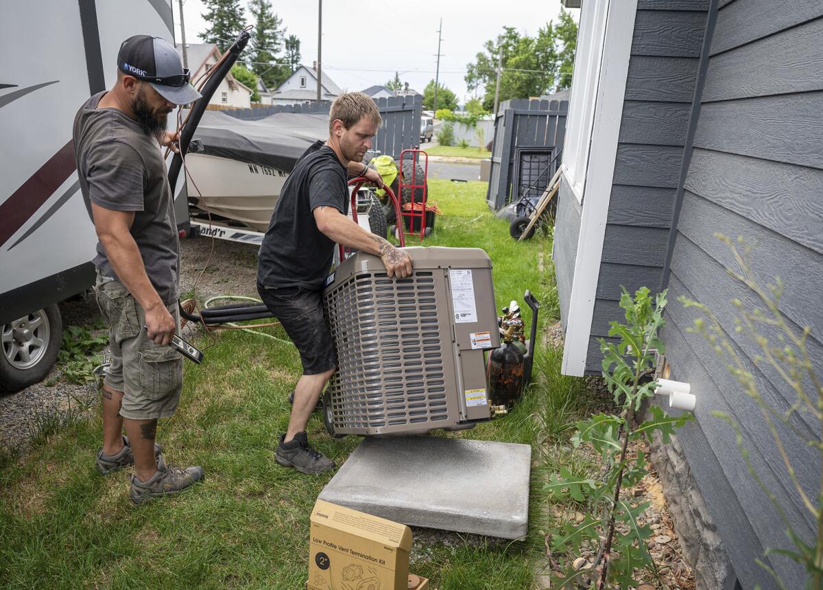 Carl Rocha, left, and Patrick Plummer, with Bills Heating & A/C Install air conditioning and a new furnace at a home on East Wabash Street, Wednesday, June 23, 2021, in Spokane, Wash. With temperatures forecast to hit over 100 degrees by Sunday, a rush of customers are keeping local A/C installers busy. (Colin Mulvany/The Spokesman-Review via AP)