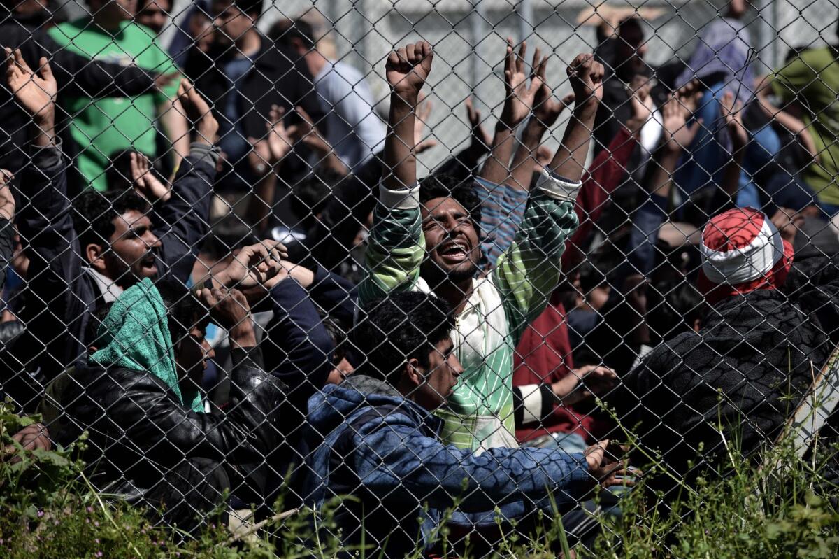 Men hold their hands up behind a fence as Pakistani and Afghan migrants protest at the Moria detention center in Mytilene on the Greek island of Lesbos on April 5 against deportation to Turkey. (Aris Messinis / AFP/Getty Images)