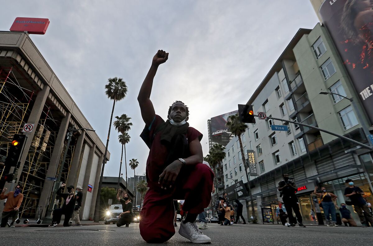 A man kneels in the street and holds his fist up.