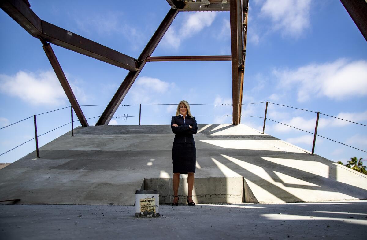 A blond woman in a business suit stands with arms crossed at the Orange County Museum of Art construction site.
