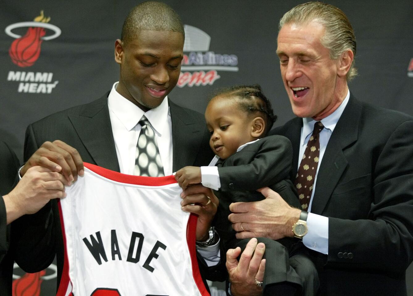 Dwyane Wade, left, former Marquette point guard and the fifth overall selection in the 2003 NBA draft, gets a little help holding up his jersey from his son Zaire, as Miami Heat coach Pat Riley, right, holds him during a news conference introducing Wade in Miami.