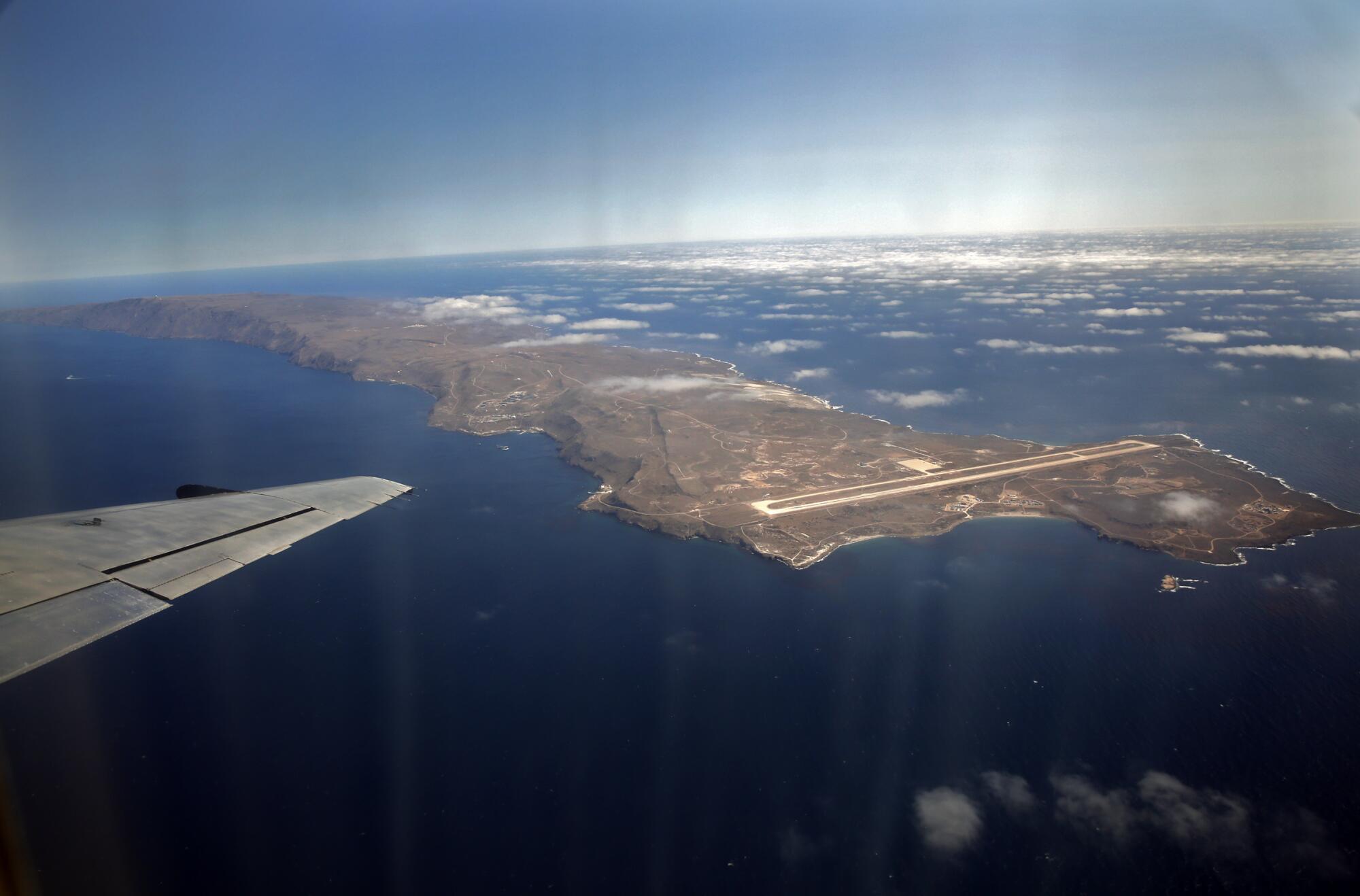 A dry island in front of an airplane wing surrounded by clouds.