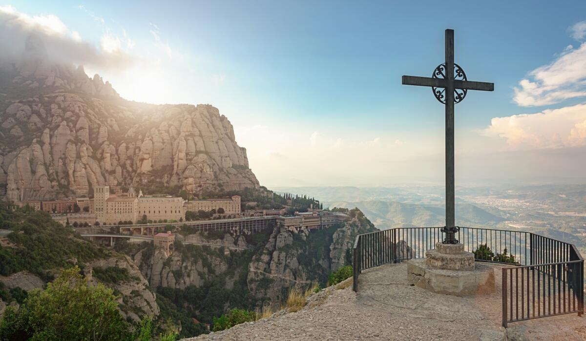A cross and Benedictine abbey on Montserrat mountain take on a religious glow near sunset.