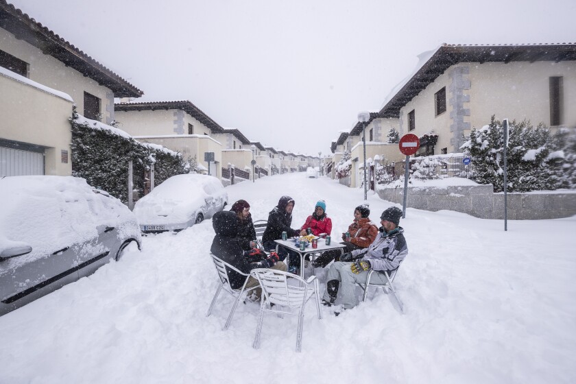 Neighbours have drinks in the middle of the street during a heavy snowfall in Bustarviejo, outskirts of Madrid, Spain, Saturday, Jan. 9, 2021. A persistent blizzard has blanketed large parts of Spain with 50-year record levels of snow, halting traffic and leaving thousands trapped in cars or in train stations and airports that suspended all services as the snow kept falling on Saturday. Half of Spain is on alert, with five provinces on their highest level of warning. (AP Photo/Bernat Armangue)