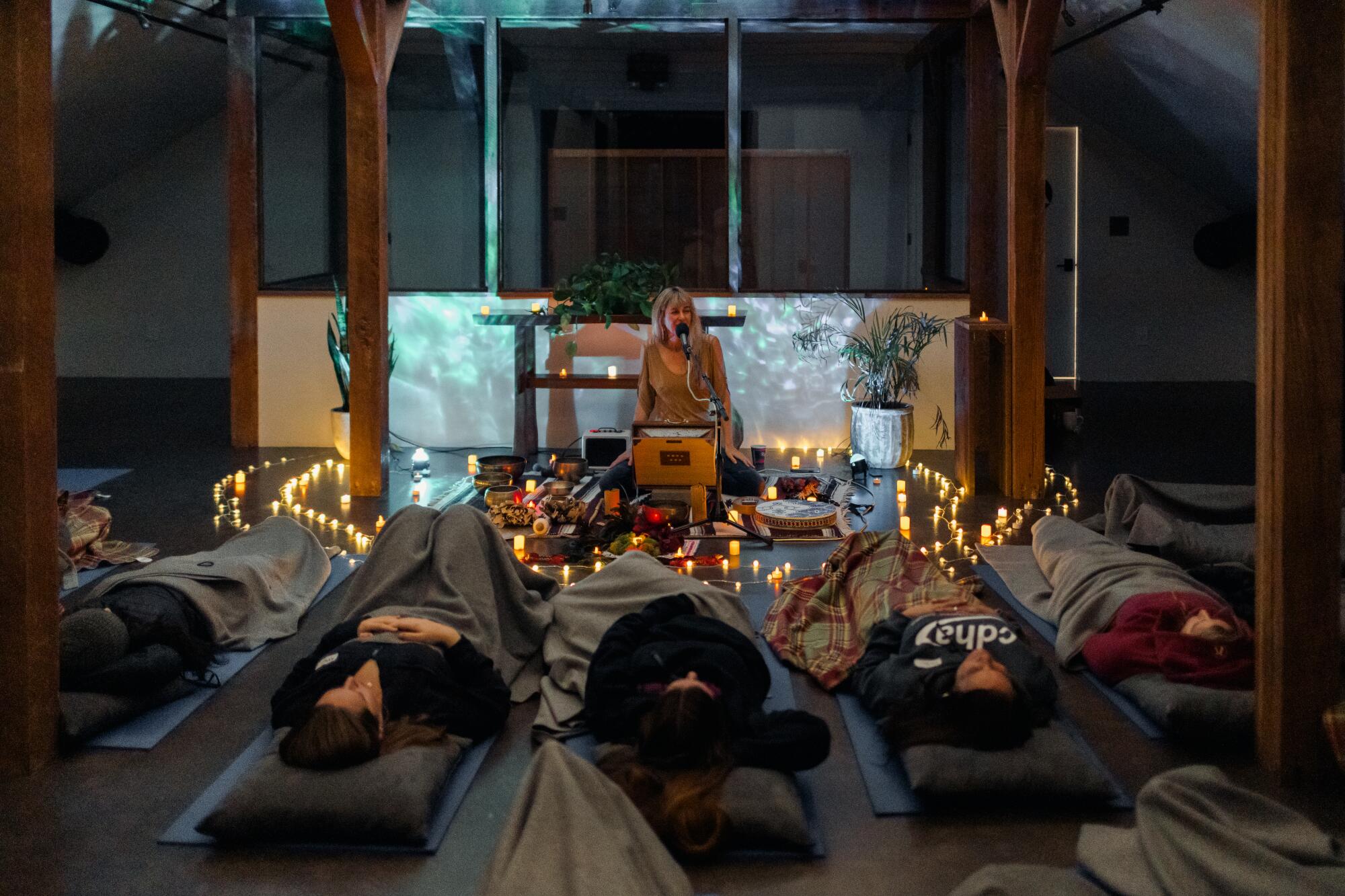 A woman sits on the ground in front of a room at a microphone while other people lay down on the ground in front of her.