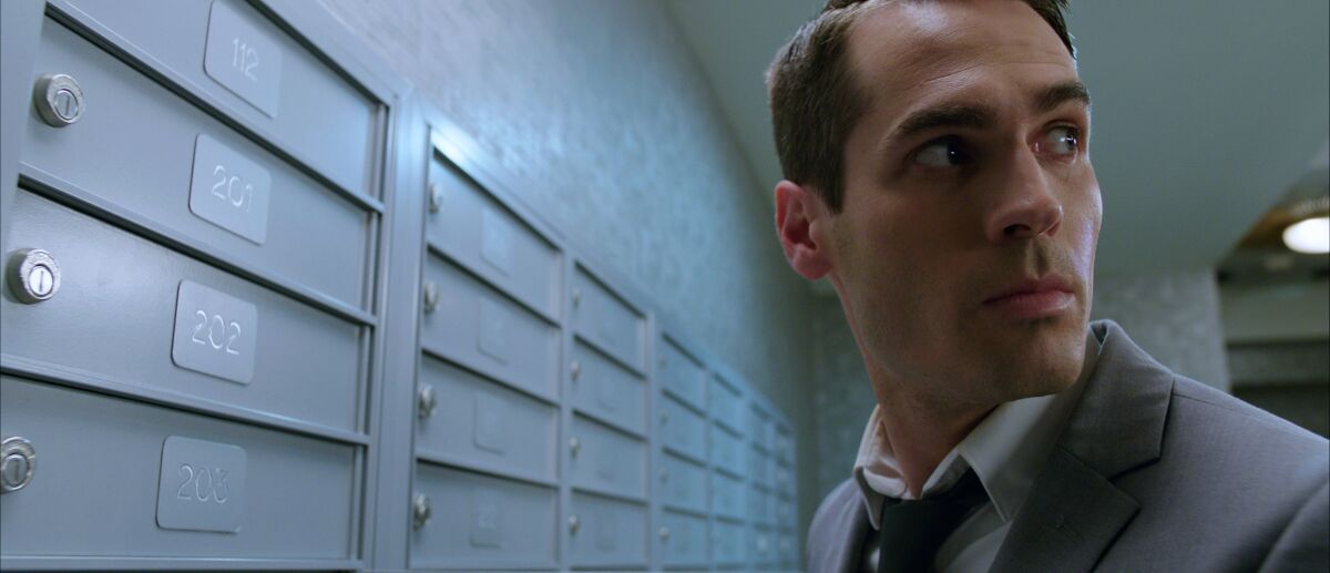 A man standing in front of post office boxes looks nervously over one shoulder.