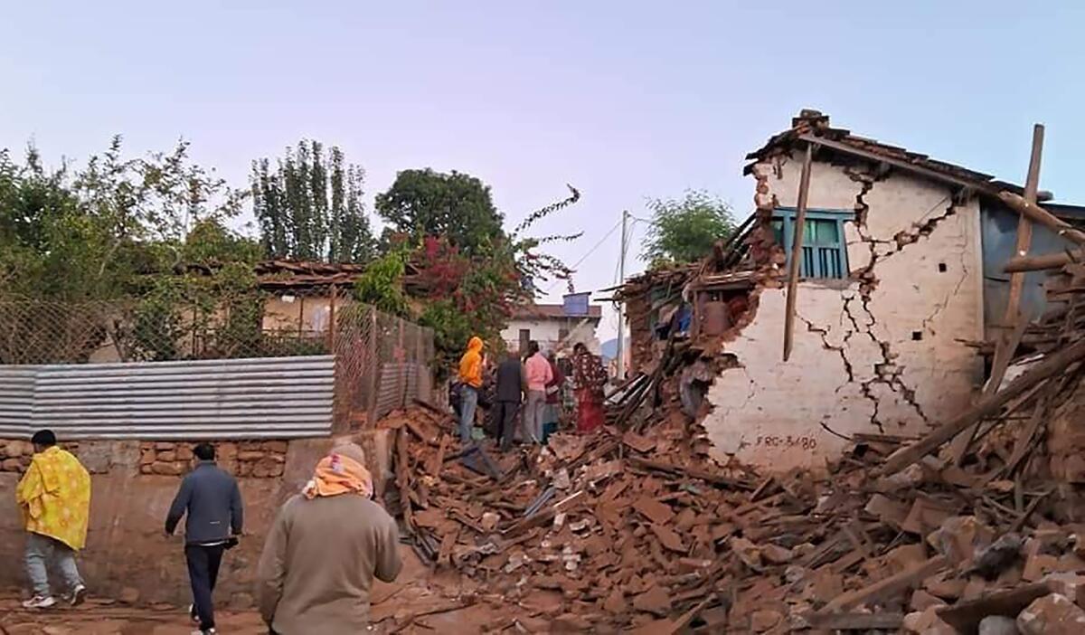 People stand outside a house, half of which has been reduced to rubble by an earthquake