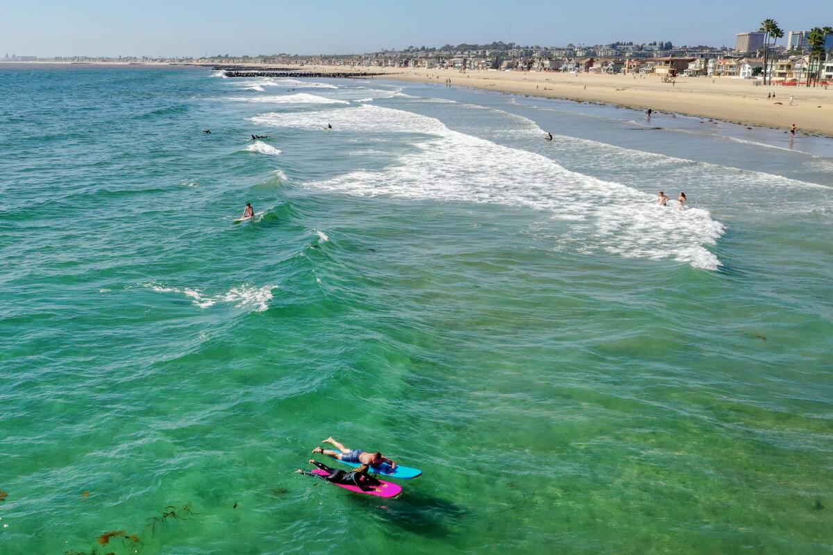 An aerial view of surfers, one on a pink board and one on a green one, in Newport Beach. 