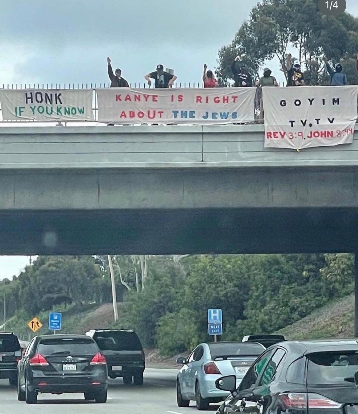 Cars driving by an overpass where people have hung antisemitic banners