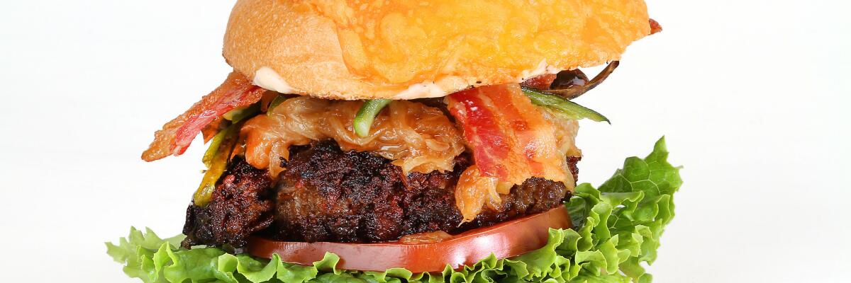 A hamburger with lettuce, a slice of tomato, cheese, onions, sliced chiles and bacon.