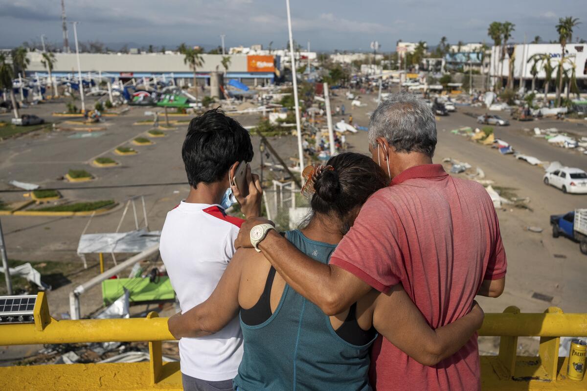 Three people hug looking down at roadside storm damage