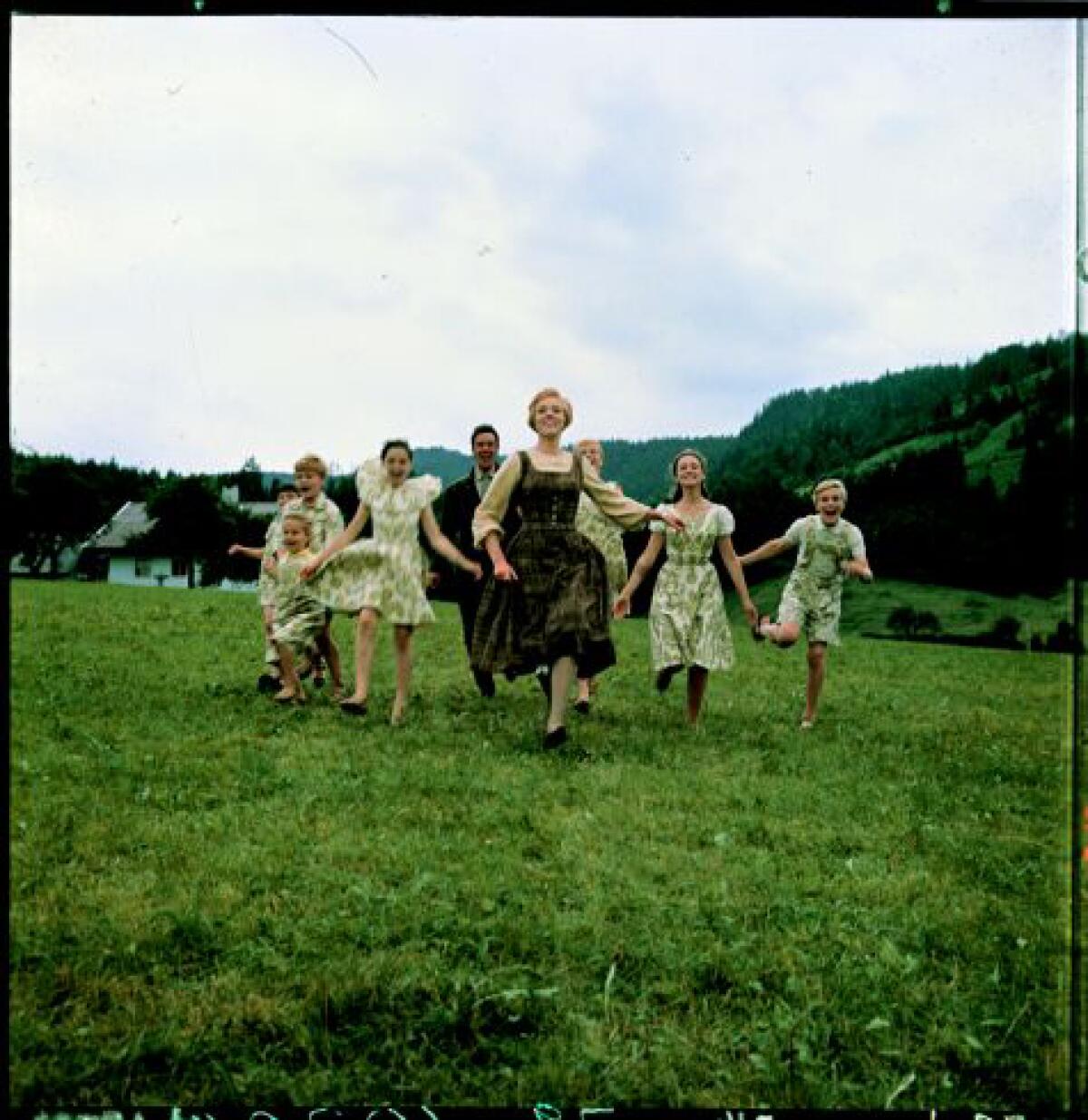 Children run in a field, led by a woman 