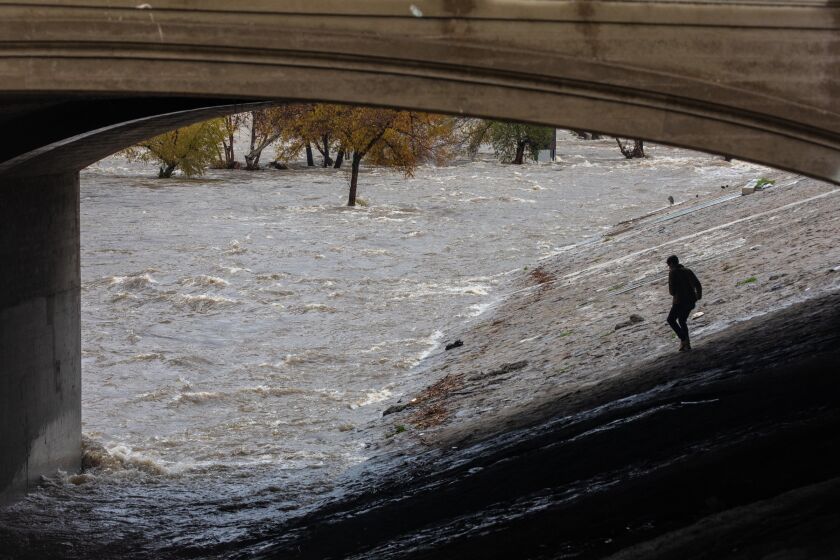 Atwater, CA - January 05: A man takes a closer look at rain-swollen LA River raging under Glendale Blvd. on Thursday, Jan. 5, 2023 in Atwater, CA. (Irfan Khan / Los Angeles Times)