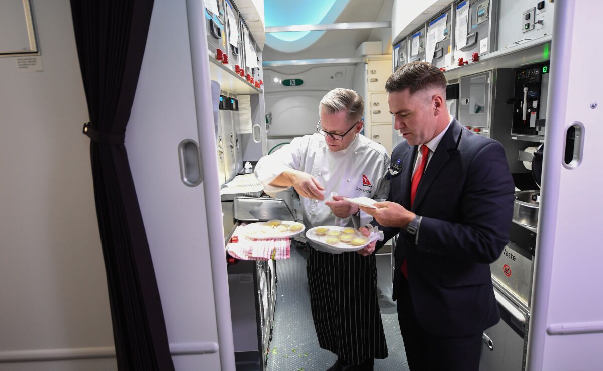 Two crew members, one in a chef's jacket and the other in a suit, in the galley with plates of food.