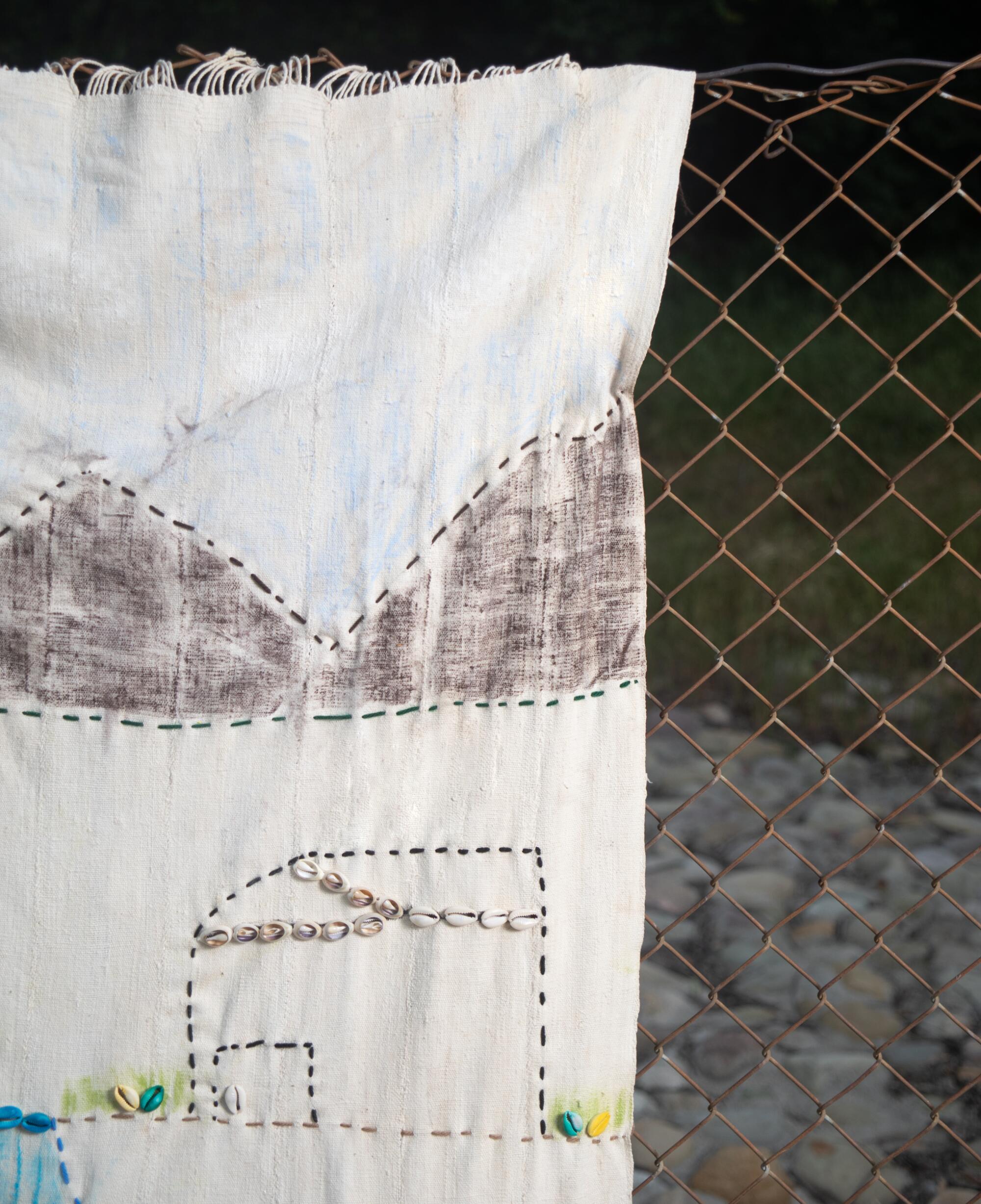 A detail of a textile showing a house and mountains in the distance.
