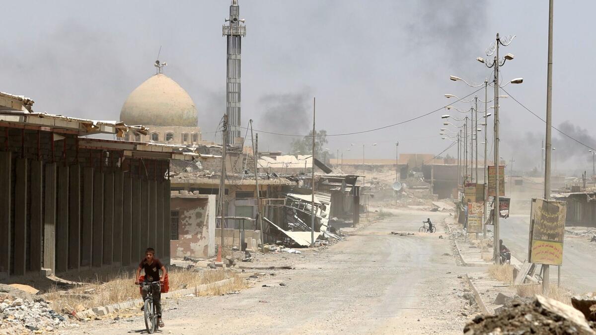 A boy rides a bicycle in west Mosul's Saha neighborhood on May 29, 2017, as smokes billows during ongoing battles between Iraqi forces and Islamic State militants.