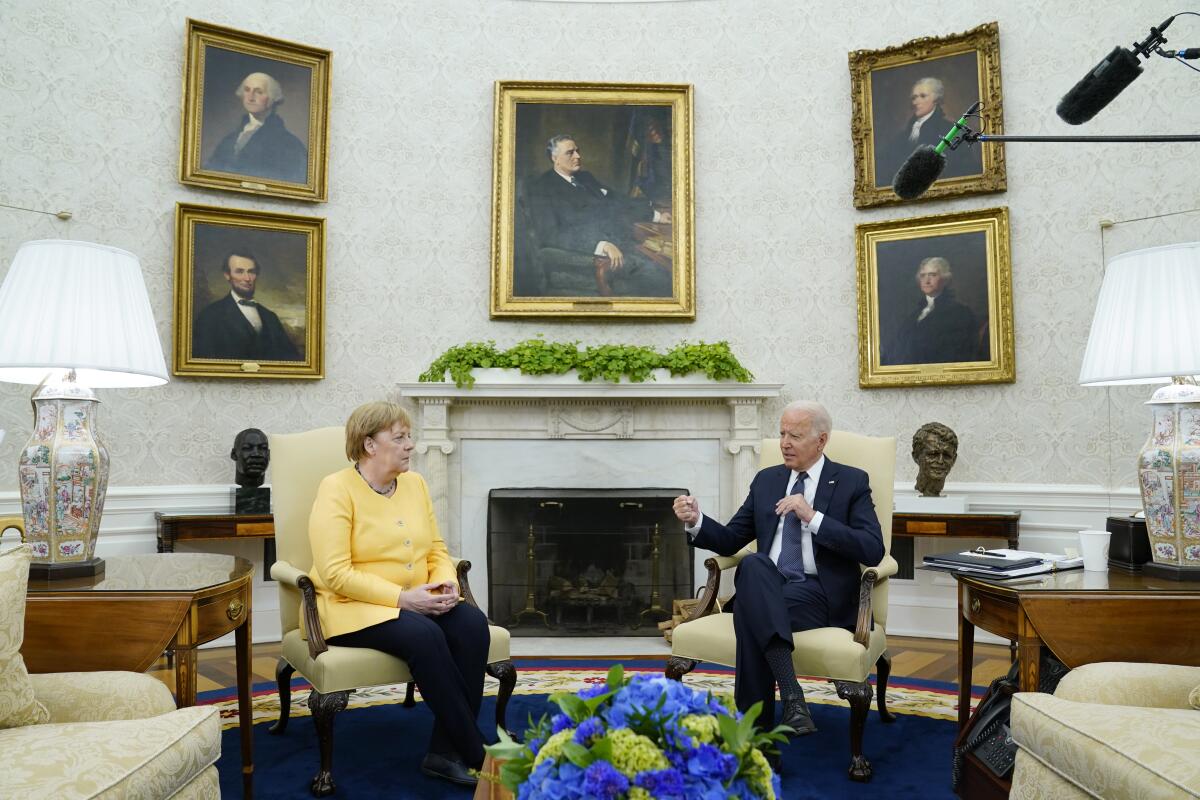 German Chancellor Angela Merkel sits in a chair next to President Biden.