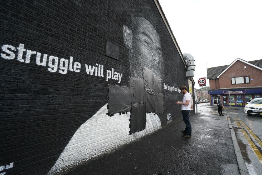 Ed Wellard, from Withington, tapes bin liners across offensive wording on the mural of Manchester United striker and England player Marcus Rashford on the wall of the Coffee House Cafe on Copson Street, which appeared vandalised the morning after the England soccer team lost the Euro 2021 final against Italy, in Withington, Manchester, England, Monday, July 12, 2021. British Prime Minister Boris Johnson has condemned the racist abuse directed at three Black England players who missed their penalties in the team’s shootout loss to Italy in the final of the European Championship on Sunday. Johnson tweeted that “those responsible for this appalling abuse should be ashamed of themselves.” Marcus Rashford’s penalty hit the post and spots kicks from Bukayo Saka and Jadon Sancho were saved by Italy's goalkeeper. (Peter Byrne/PA via AP)