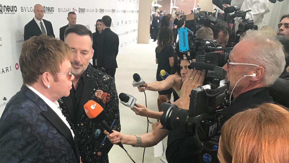 Elton John, left, and David Furnish speak to reporters upon arriving at the EJAF Oscars viewing party.