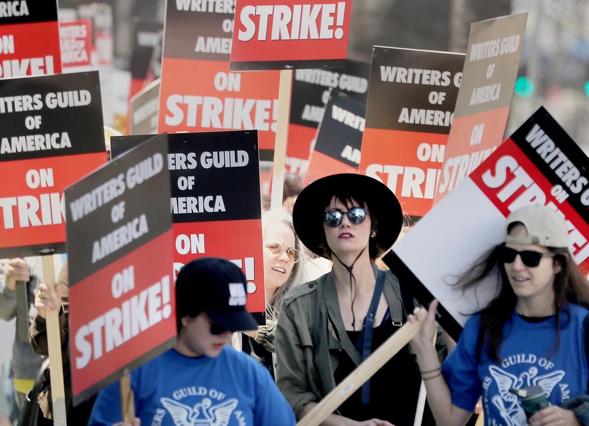 people picketing with signs reading "writers guild of america on strike!"