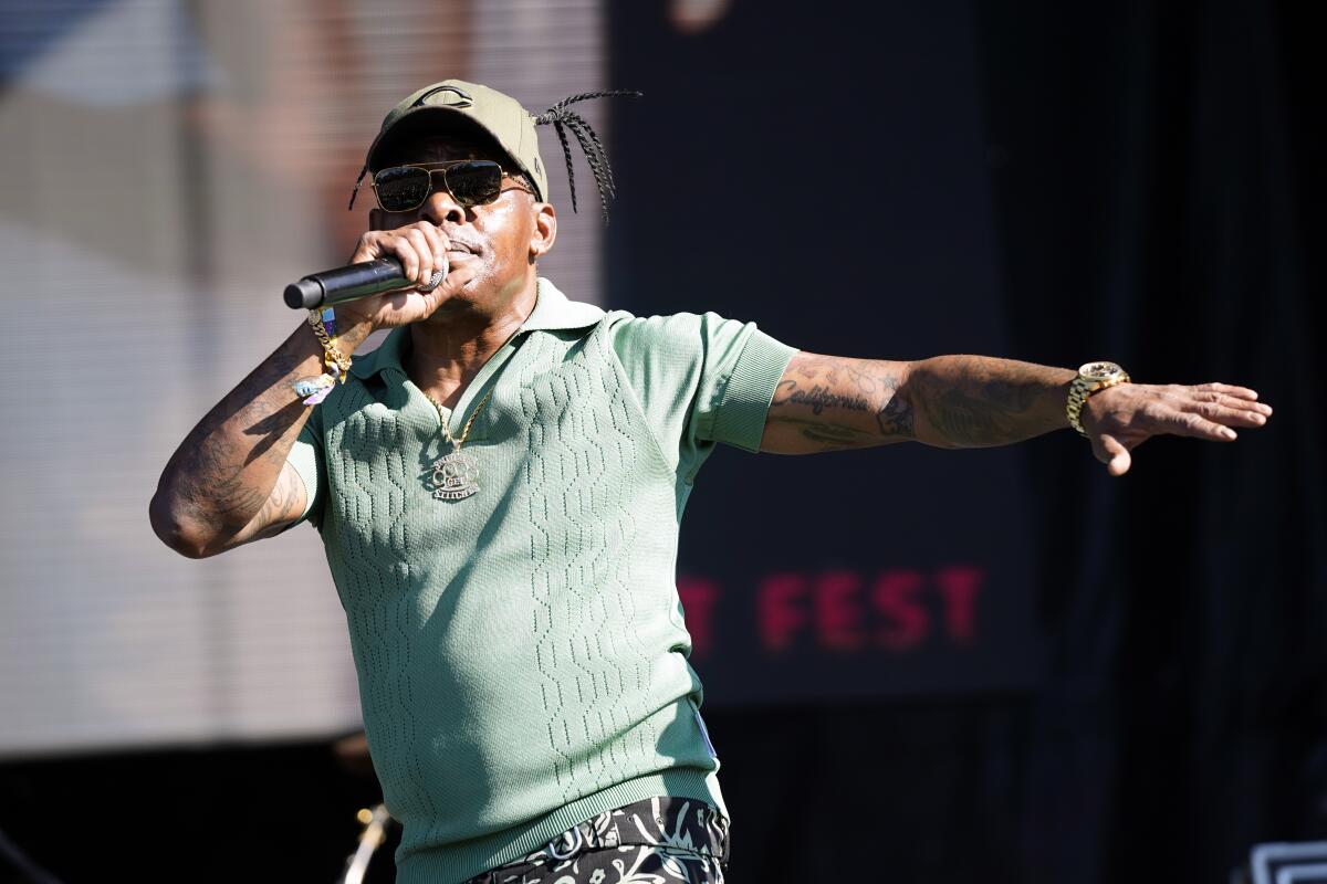 Coolio raps onstage in a seafoam green shirt and baseball cap, one hand extended, the other holding a microphone to his mouth