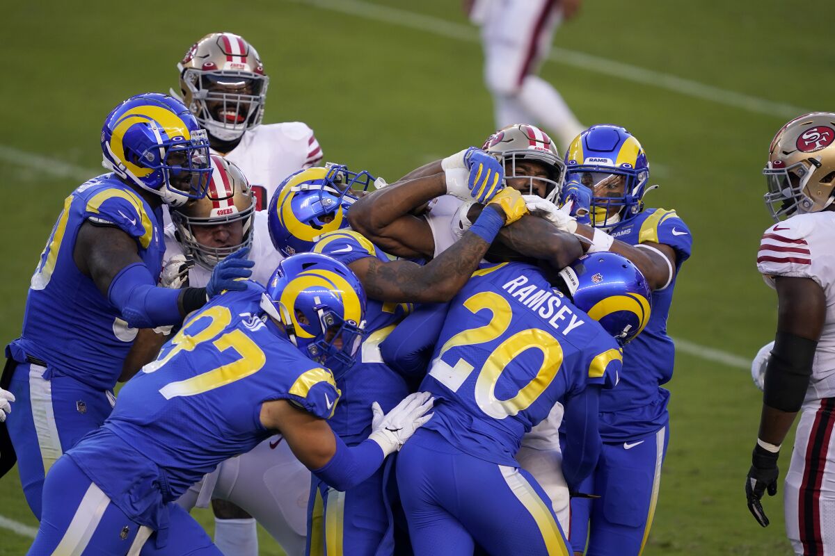 San Francisco 49ers running back Raheem Mostert, center, is tackled by Rams defenders.