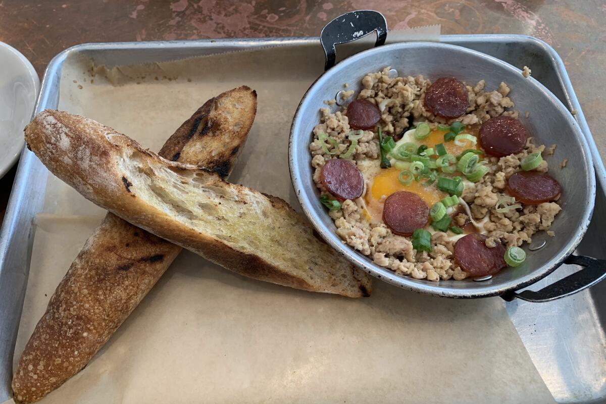 Two toasted baguette slices next to a dish filled with rice, egg, sausage, green onion and more.