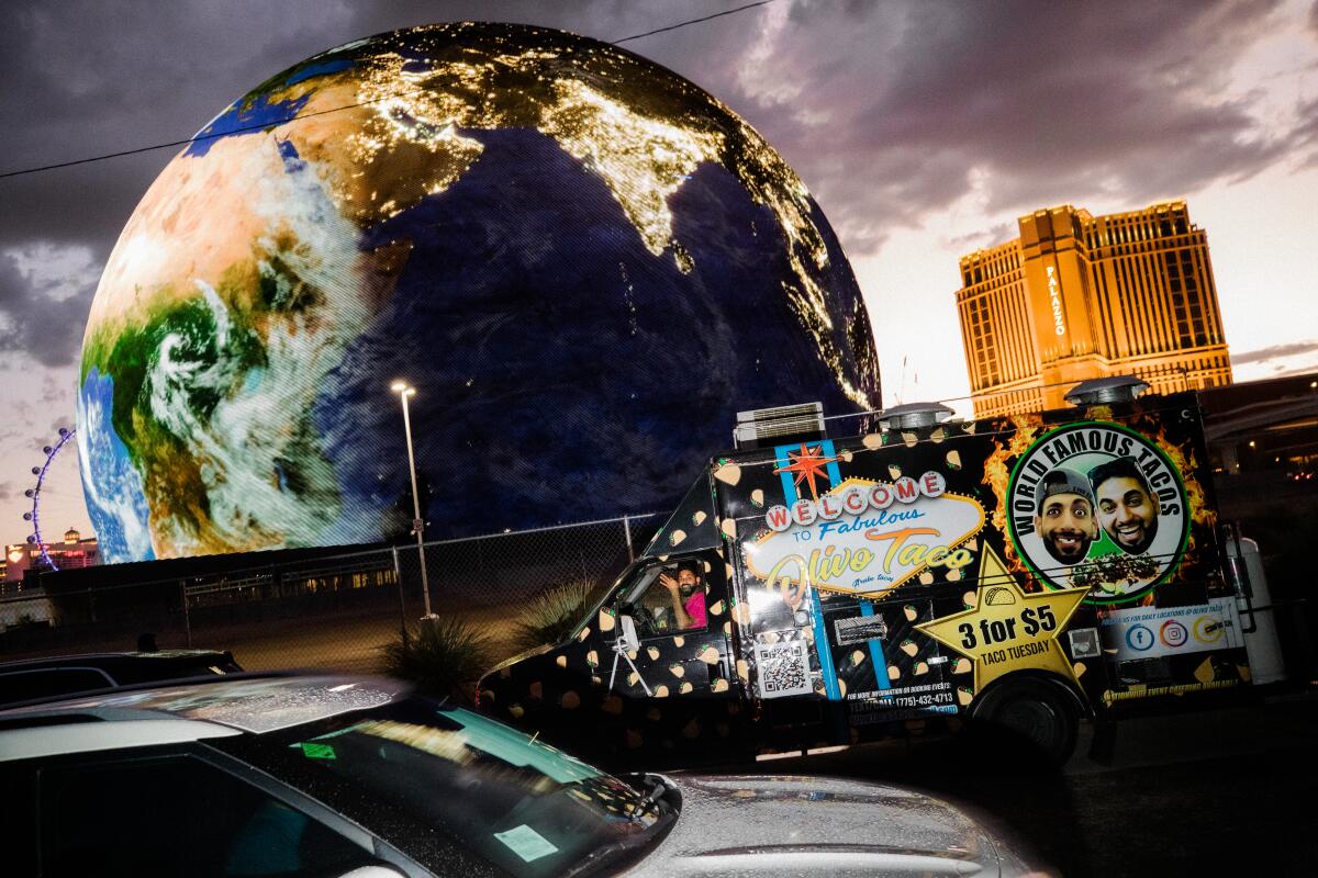 A large round display of the Earth over the a taco truck painted with Las Vegas Strip against stormy clouds
