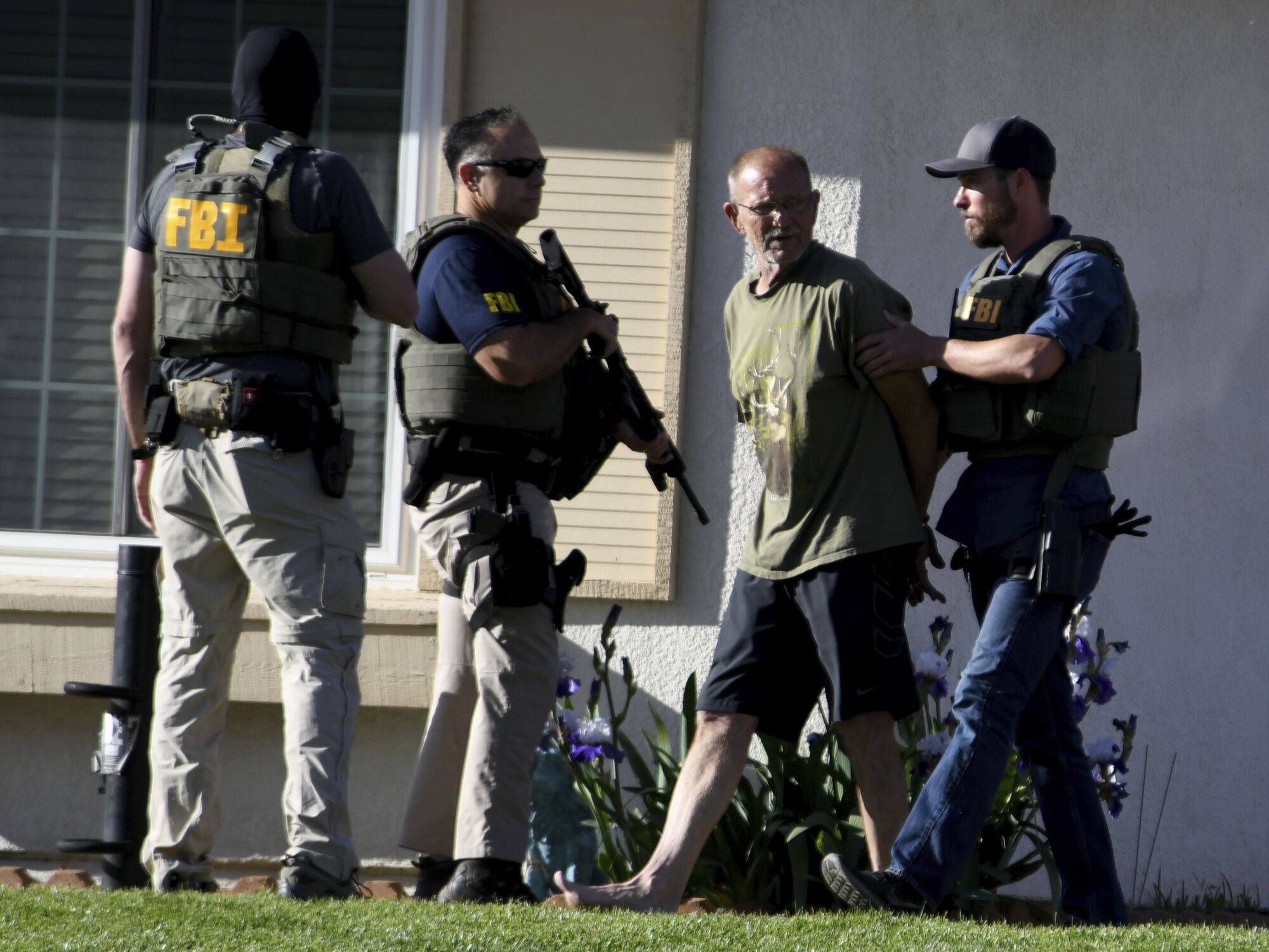 A handcuffed man is escorted by armed FBI agents