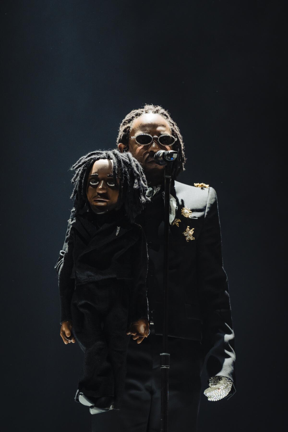 A rapper onstage with a ventriloquist dummy that looks like him.