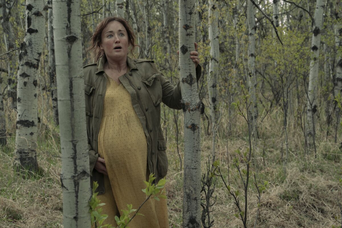 A pregnant woman in a green jacket and long yellow dress standing in a forest