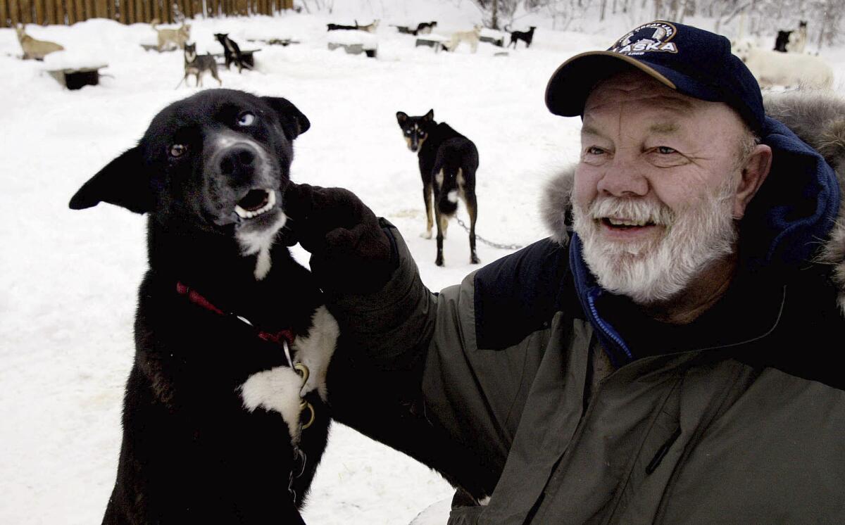 A man in a heavy coat smiles with a black dog 