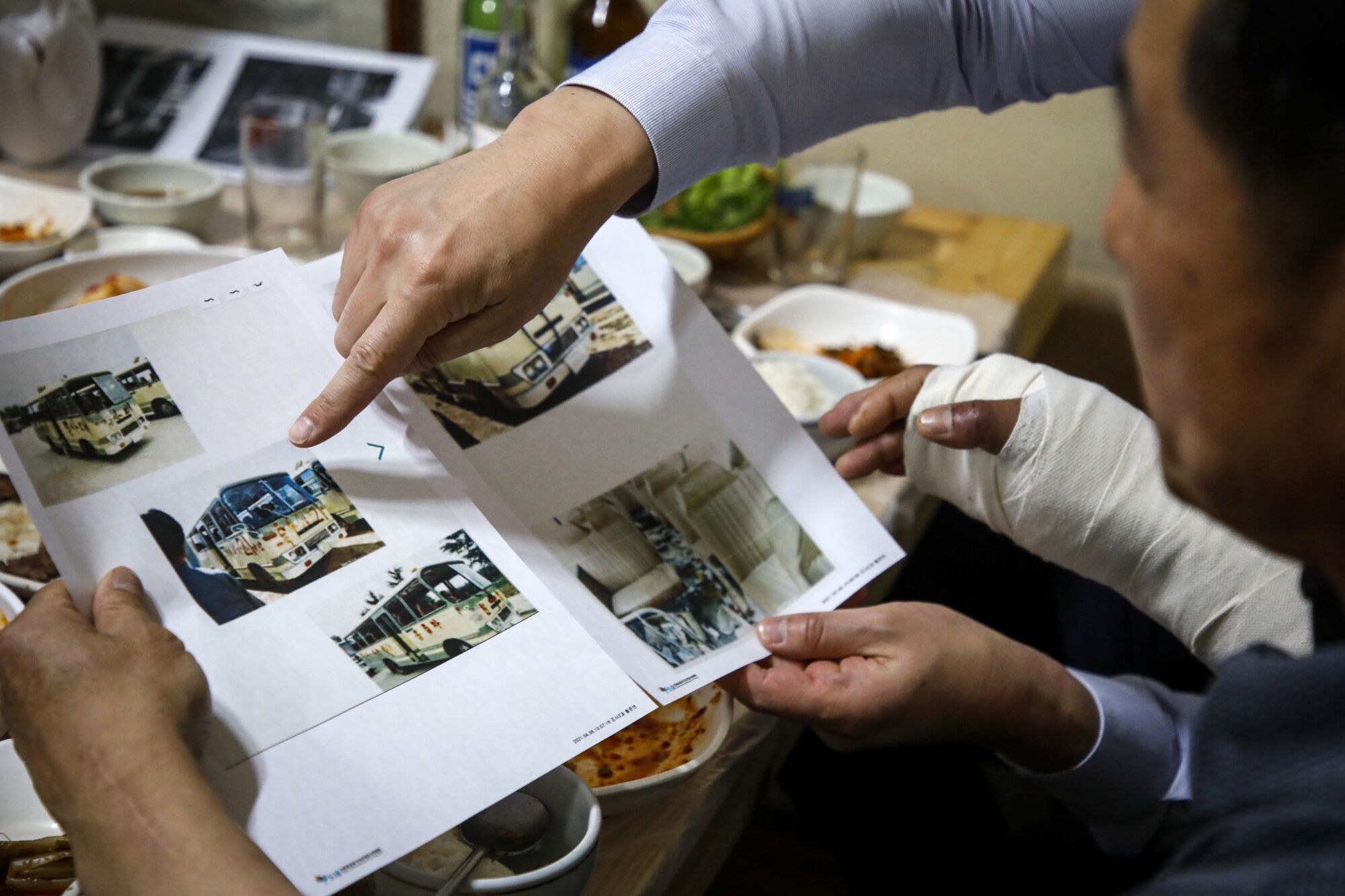 A finger points at a picture on a page with several photographs while a seated man looks at the page