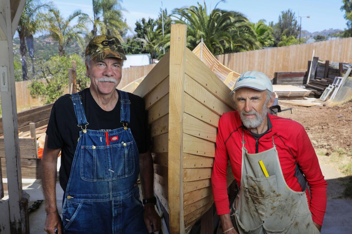 Two men pause next to the boat they are building.