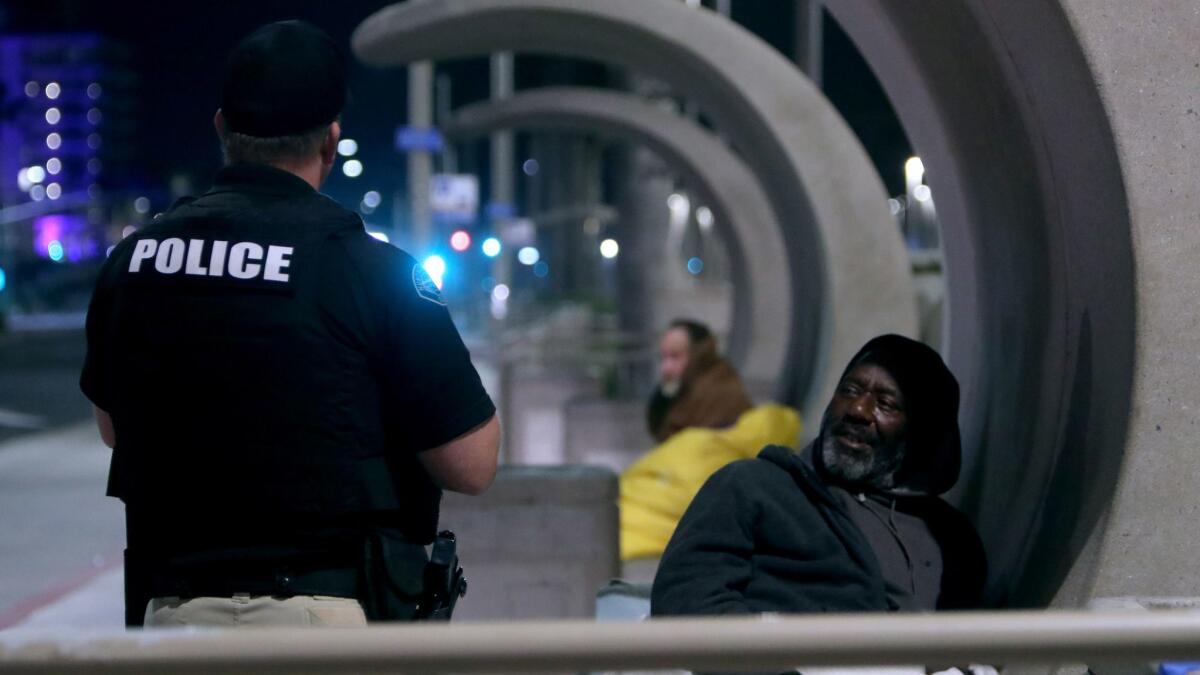 Huntington Beach Homeless Task Force Officer Gabe Ricci speaks with a homeless man who was sleeping on a bench on Pacific Coast Highway on Feb. 13.